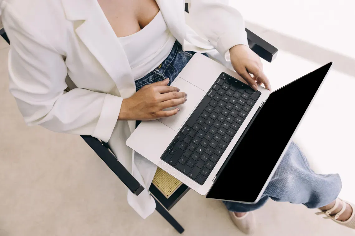 A woman sitting in a chair with an open laptop on her lap.