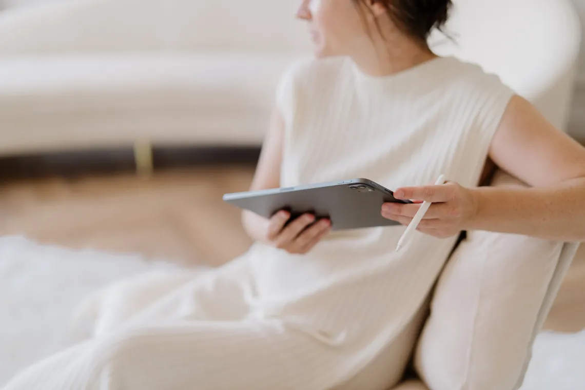 A Woman sitting in an upholstered chair holding a tablet and a stylus.