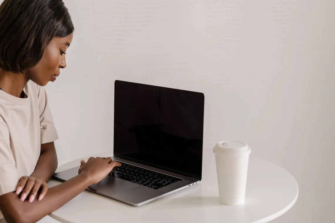A woman sitting at a table typing on a laptop, coffee nearby.
