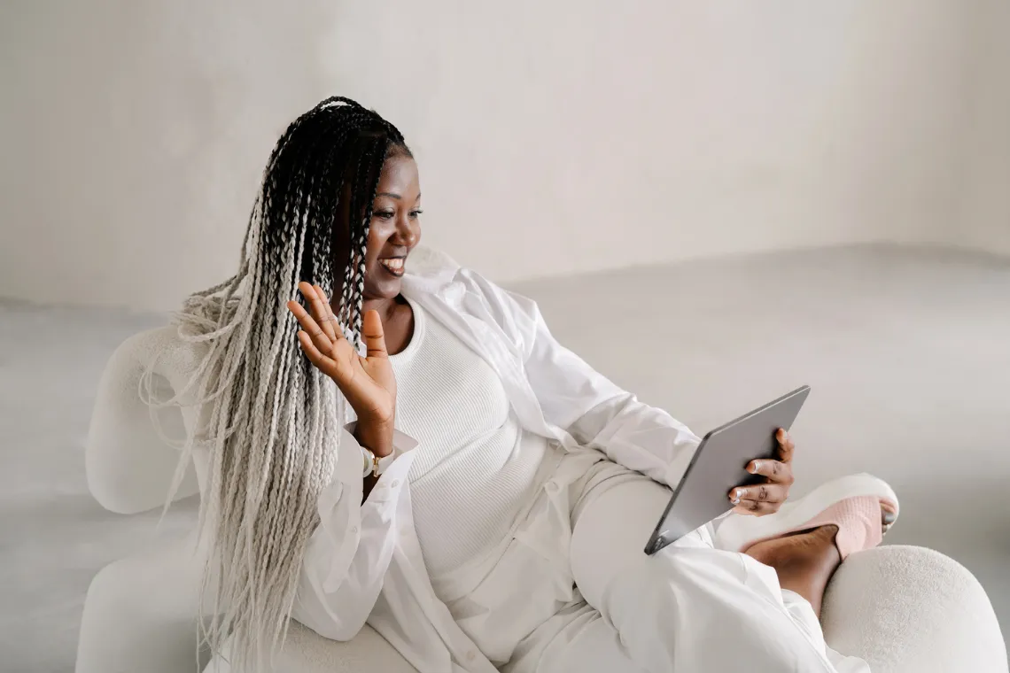 Woman sitting on a sofa with a tablet in hand, on a video call.