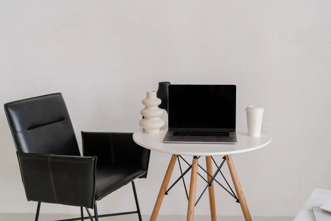 Table with an open laptop, coffee cup and vases on top, chair next to it.