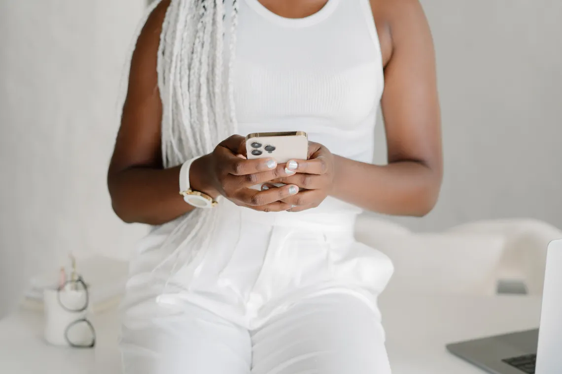 Woman sitting on a desk with phone in hand.