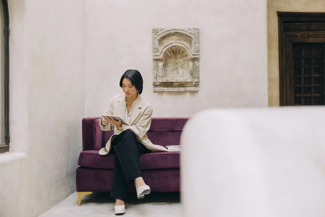 A woman sitting on a sofa with a tablet in hands.