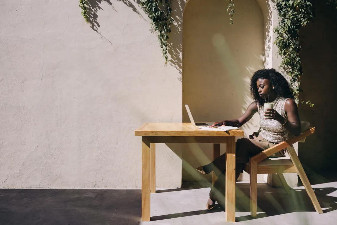 A woman sitting at a table with an open laptop, reading a Kit review while drinking a matcha latte.