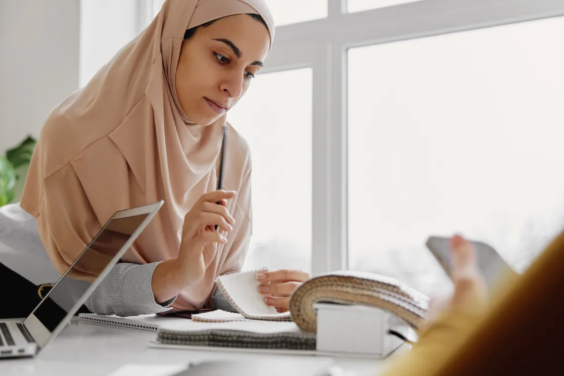 Businesswoman leaning on desk reviewing fabric samples with pencil in hand.