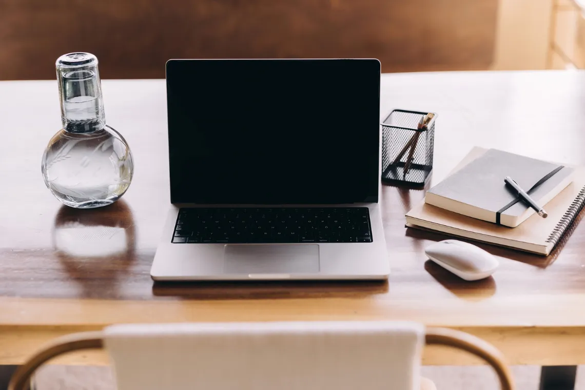 Open laptop, notebooks, pen and a water bottle on top of a table.