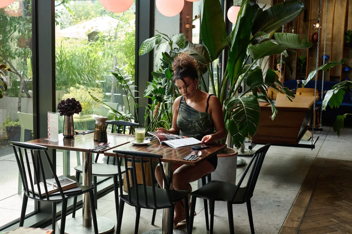 A woman sitting at a table reading a magazine.