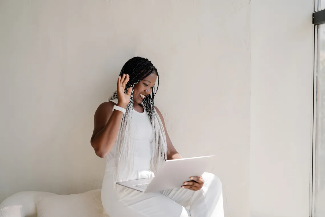 Woman leaning against a sofa with an open laptop in hands.