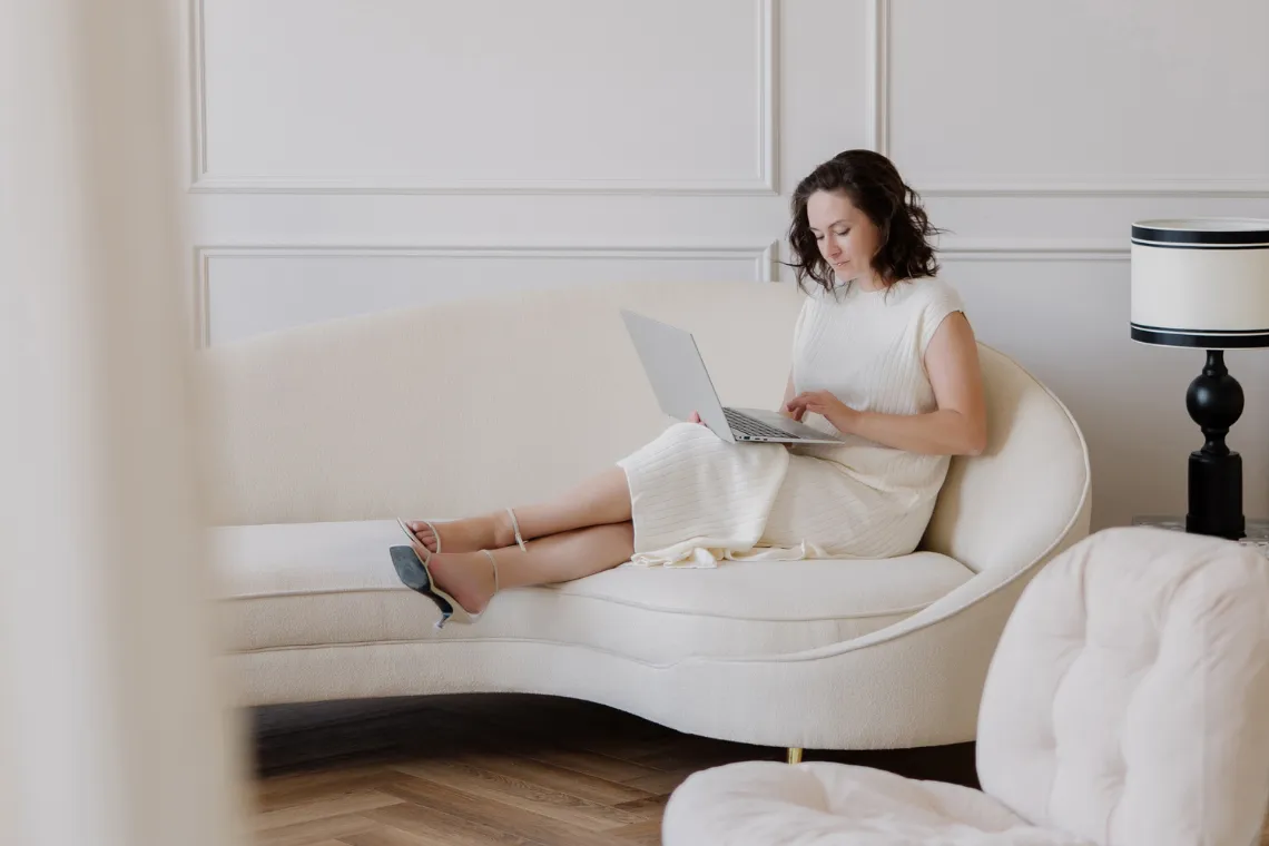 Woman sitting on a sofa, writing a blogpost on her laptop.