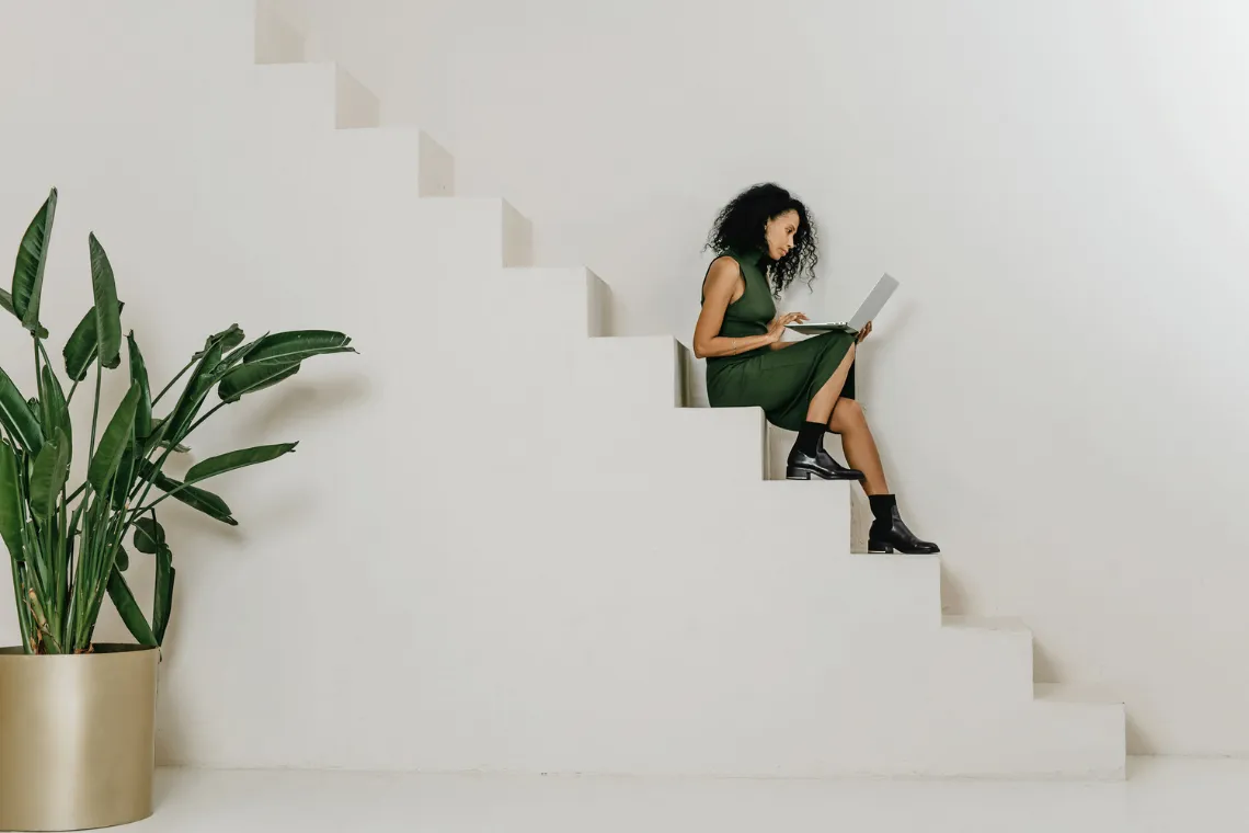 A woman sitting on a staircase typing on her laptop, reviewing her email marketing.
