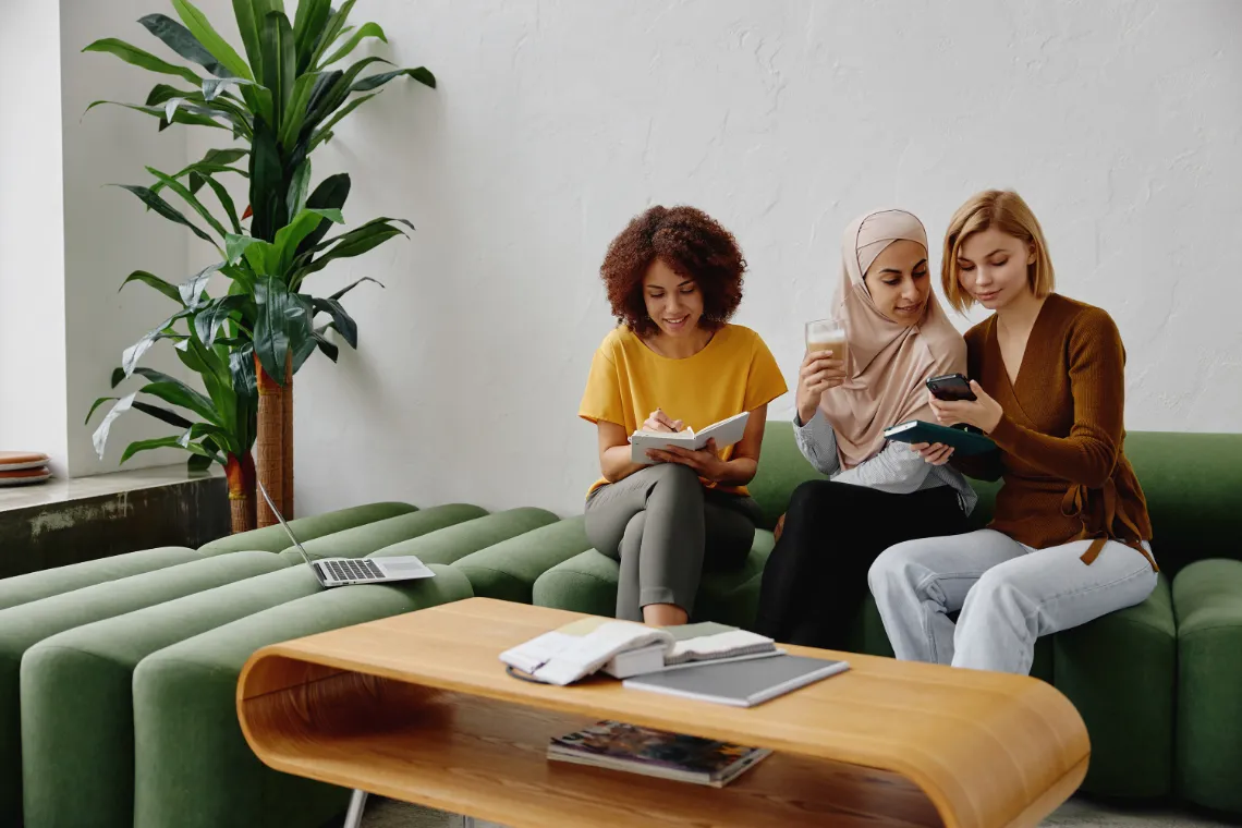Three businesswomen sitting on a couch with notebooks, phone and iced coffee.