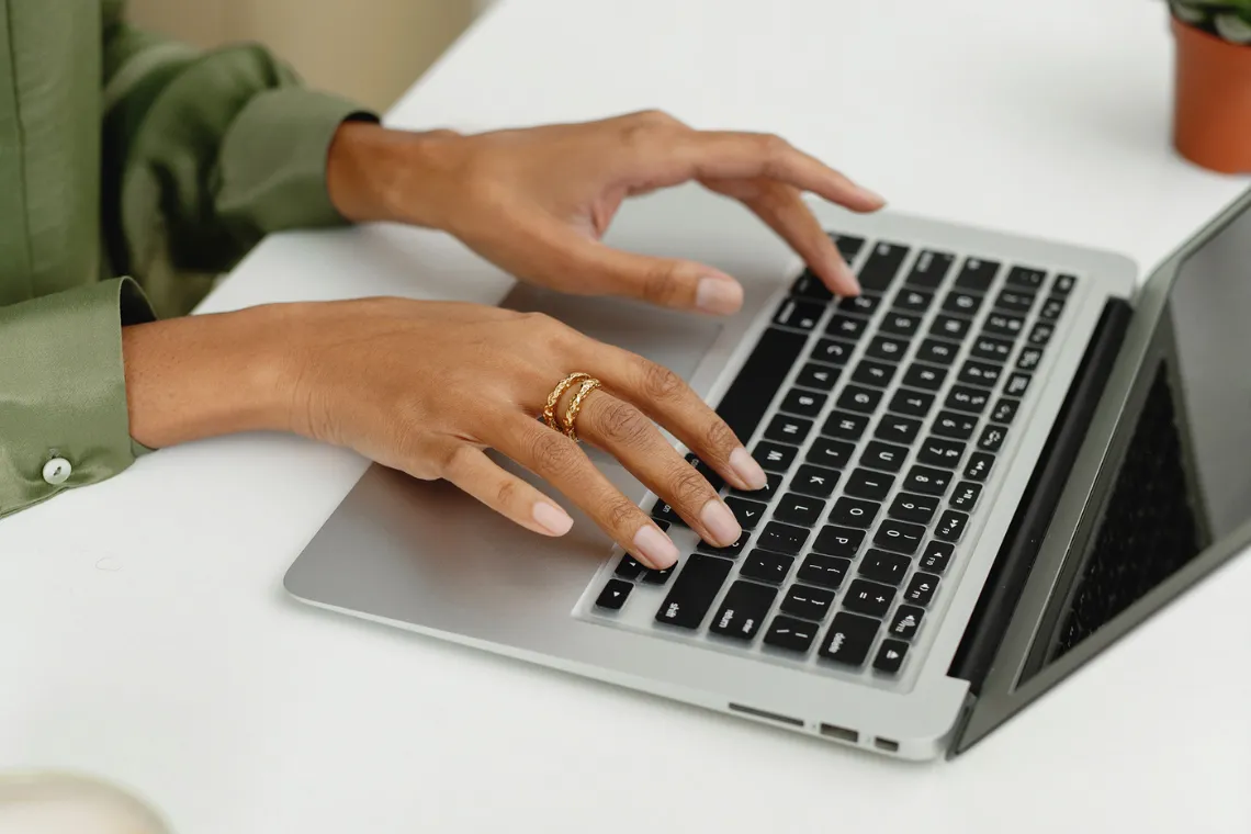Woman's hands typing on a laptop keyboard.